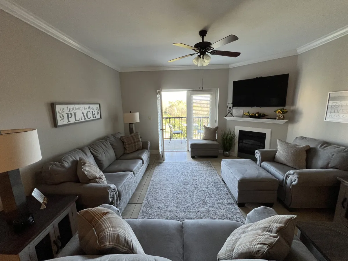 A comfortable living area featuring soft sofas, a charming fireplace, a large window that lets in natural light, and a decorative sign. The setup is inviting, cozy, and highlights views outside.