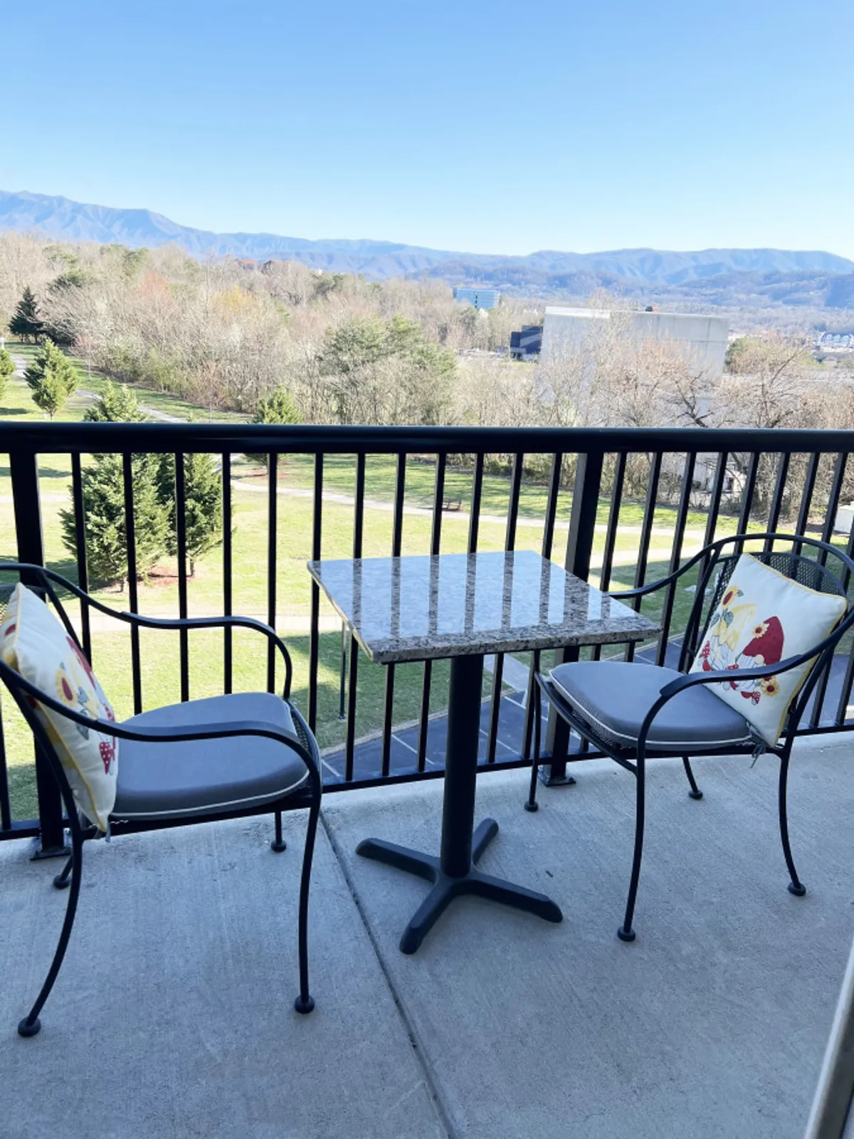 A serene balcony scene with a granite-top table, two cushioned chairs, and a stunning panoramic mountain view. The space is set for morning coffee or quiet relaxation, framed by the beauty of the Smokies.