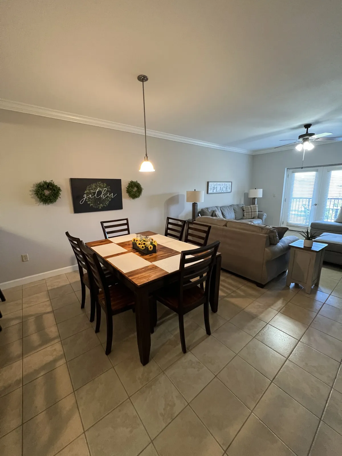 This image showcases a dining table set with a bright sunflower centerpiece, surrounded by comfortable seating, with a sofa and decorative wall art in the background. Greenery accents and warm light fixtures create an inviting, communal atmosphere ideal for family meals and social gatherings.