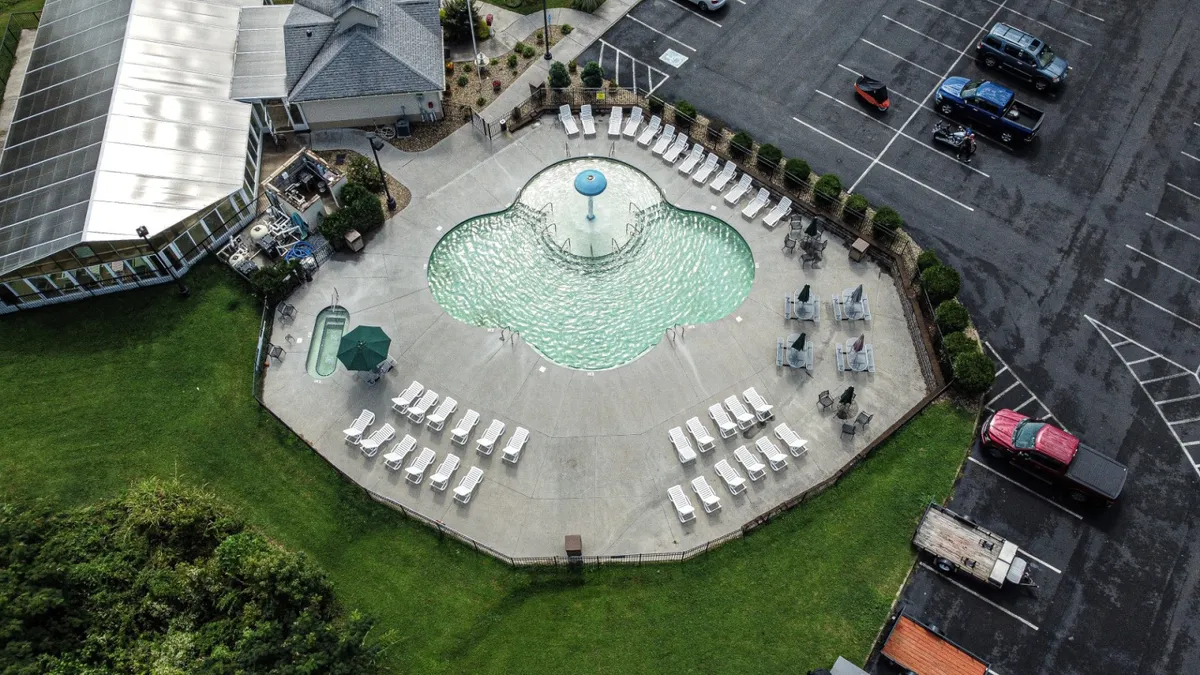 An inviting exterior pool scene features a sparkling swimming pool surrounded by lounge chairs and lush greenery. The setting is cheerful, with sunlight illuminating the water and the adjacent building structure providing a resort-like ambiance. The scene hints at relaxation, group fun, and leisurely swims.