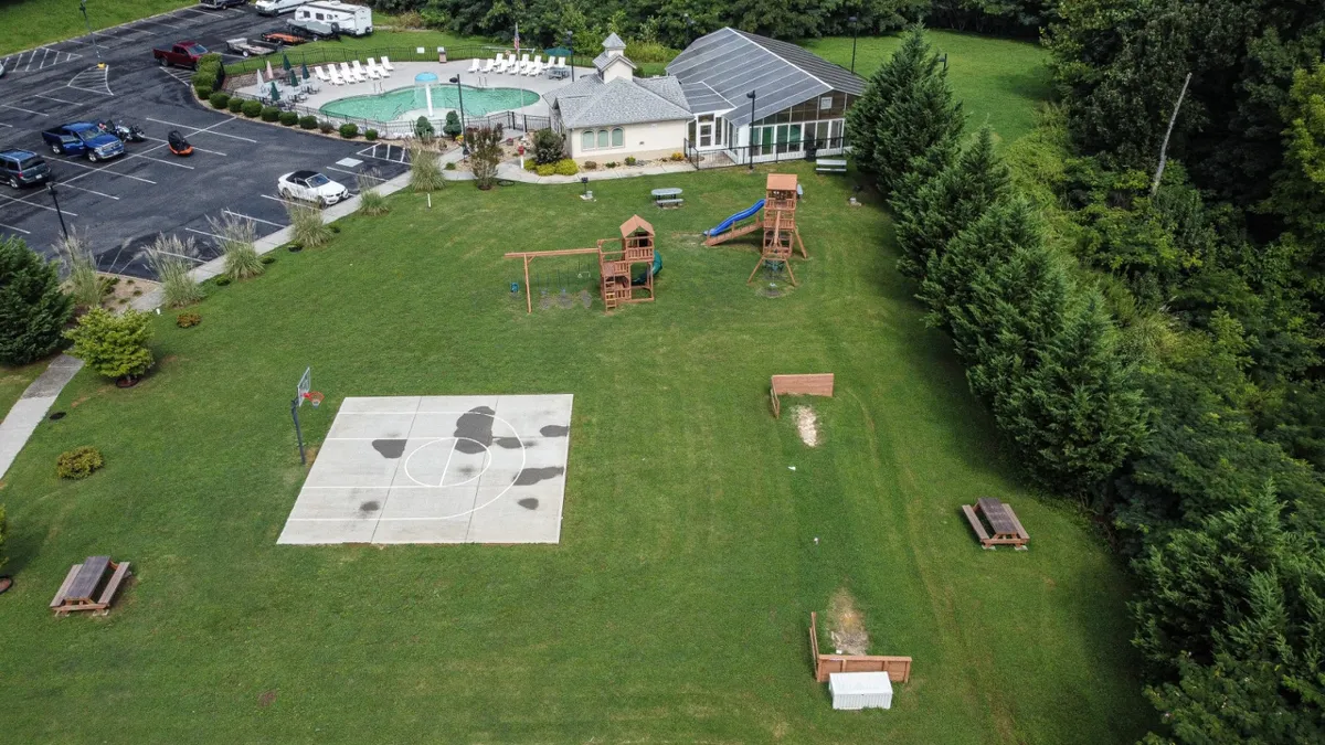 This lively exterior shot includes a basketball court, playground structures, a swimming pool, and picnic areas, bustling with families and children enjoying various recreational activities.