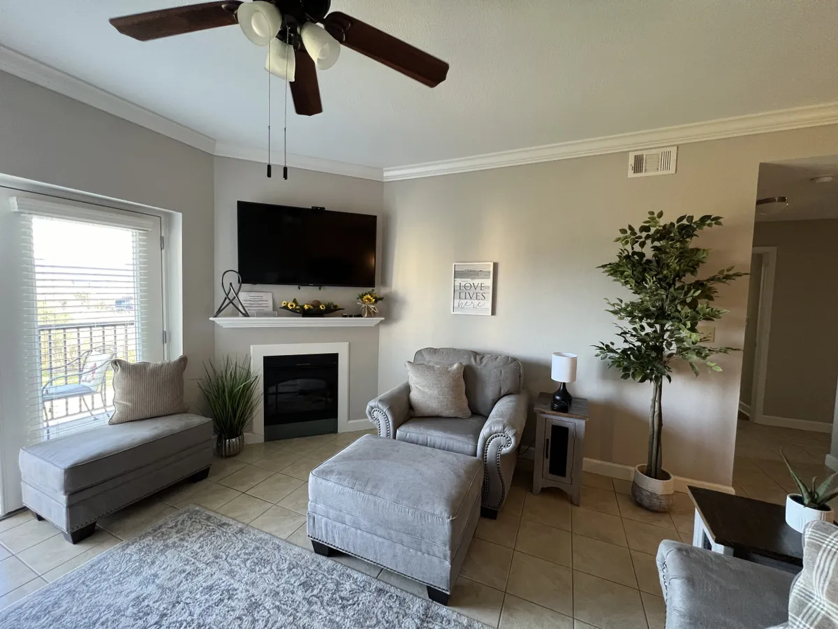 A welcoming living room with a plush sofa, a cozy fireplace, a flat screen television, and tasteful decor including a potted plant and artwork. The space is open and bright, ideal for relaxing, movie nights, and socializing.
