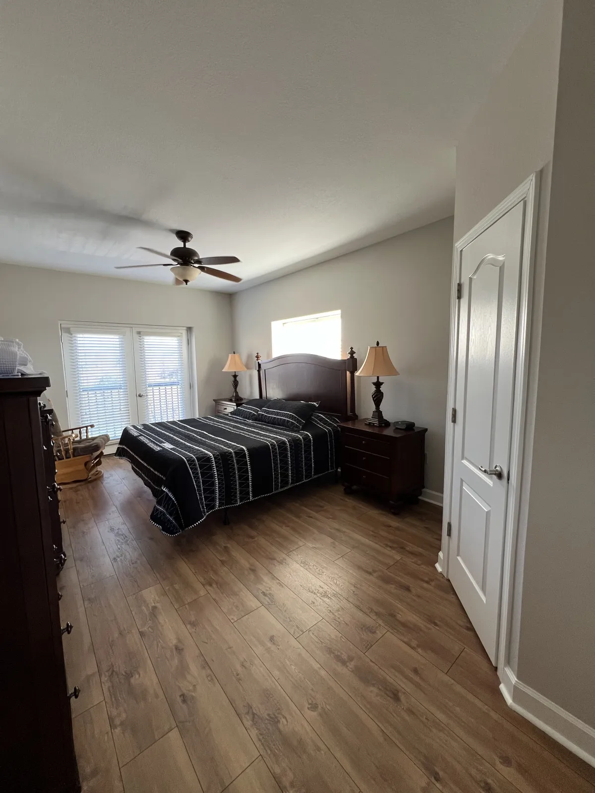 A bright and peaceful bedroom with a comfortable bed, nightstands on each side, a sunlit window, and warm wooden floors. The room is uncluttered and inviting, showcasing a space perfect for restful sleep.