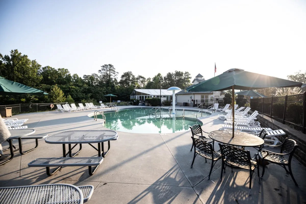 A sparkling outdoor swimming pool is surrounded by lounge chairs, tables, and umbrellas, offering an ideal setting for swimming, sunbathing, and socializing under the sun.