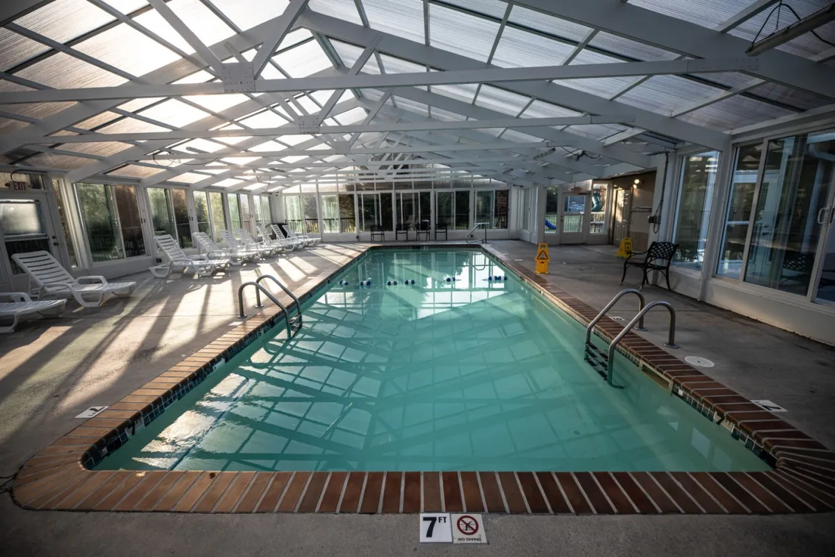 This image features a brightly lit indoor swimming pool with sunlight streaming through the roof and comfortable poolside loungers, creating an inviting space for year-round swimming and relaxation regardless of weather.