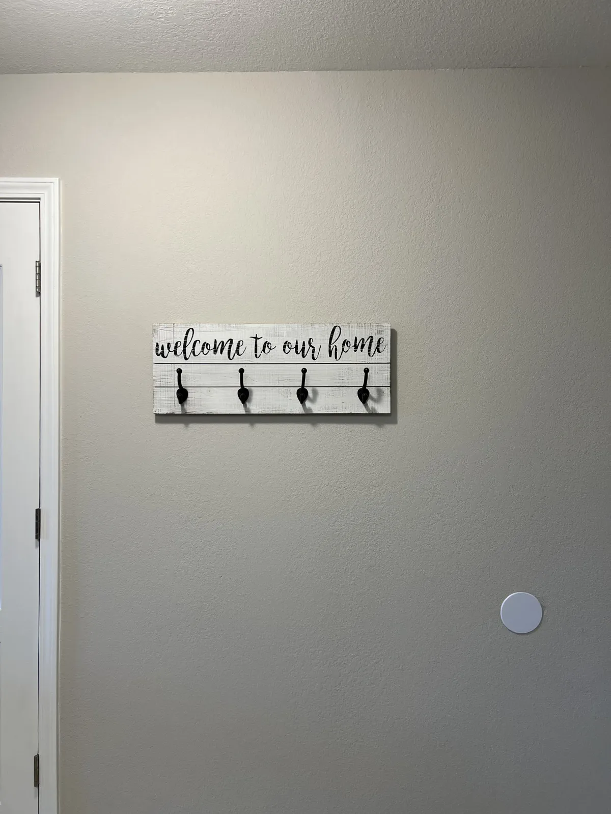 A close-up of a wooden sign that reads 'welcome to our home,' accompanied by coat hooks. This area is designed for guests to hang coats or bags upon entering, creating a warm and hospitable first impression.